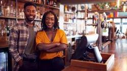Black couple who owns bar standing behind the counter smiling 